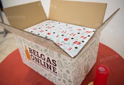 Calendario de adviento de cerveza belga de Belgas Online abierto, con sus casillas numeradas, sobre fondo rojo junto a una vela roja